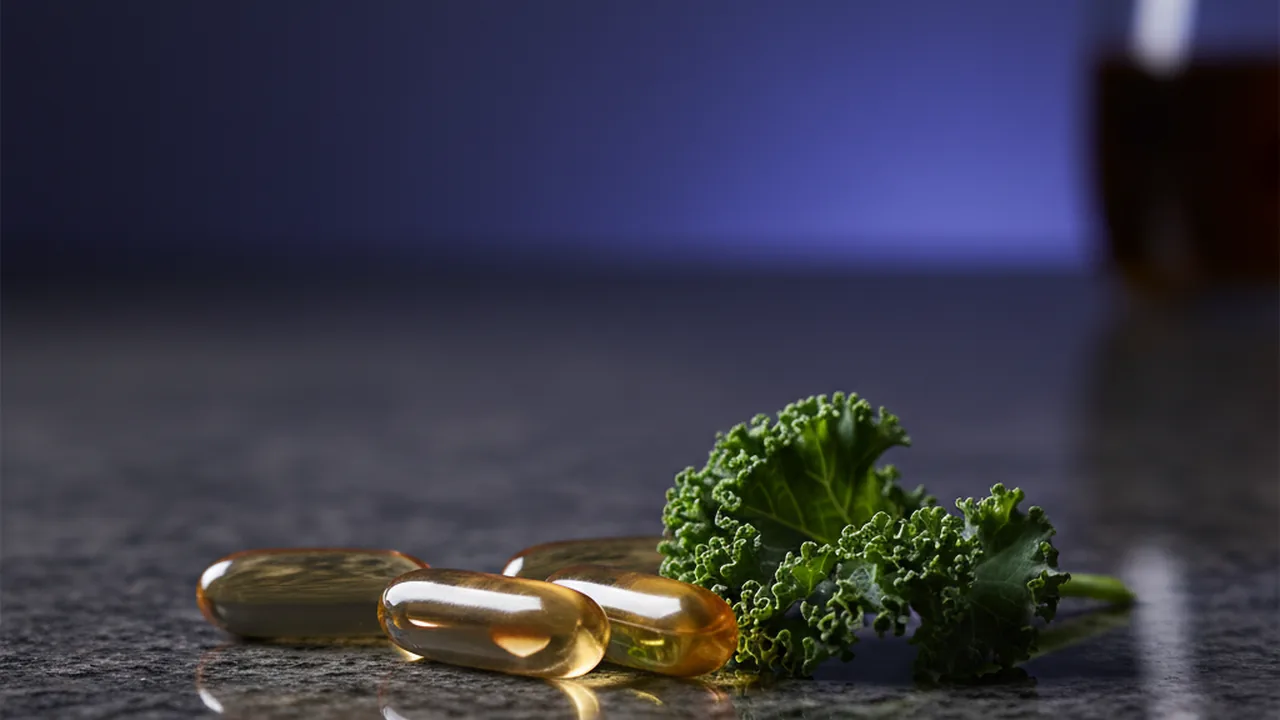 B-vitamin capsules and leafy greens on a dark surface